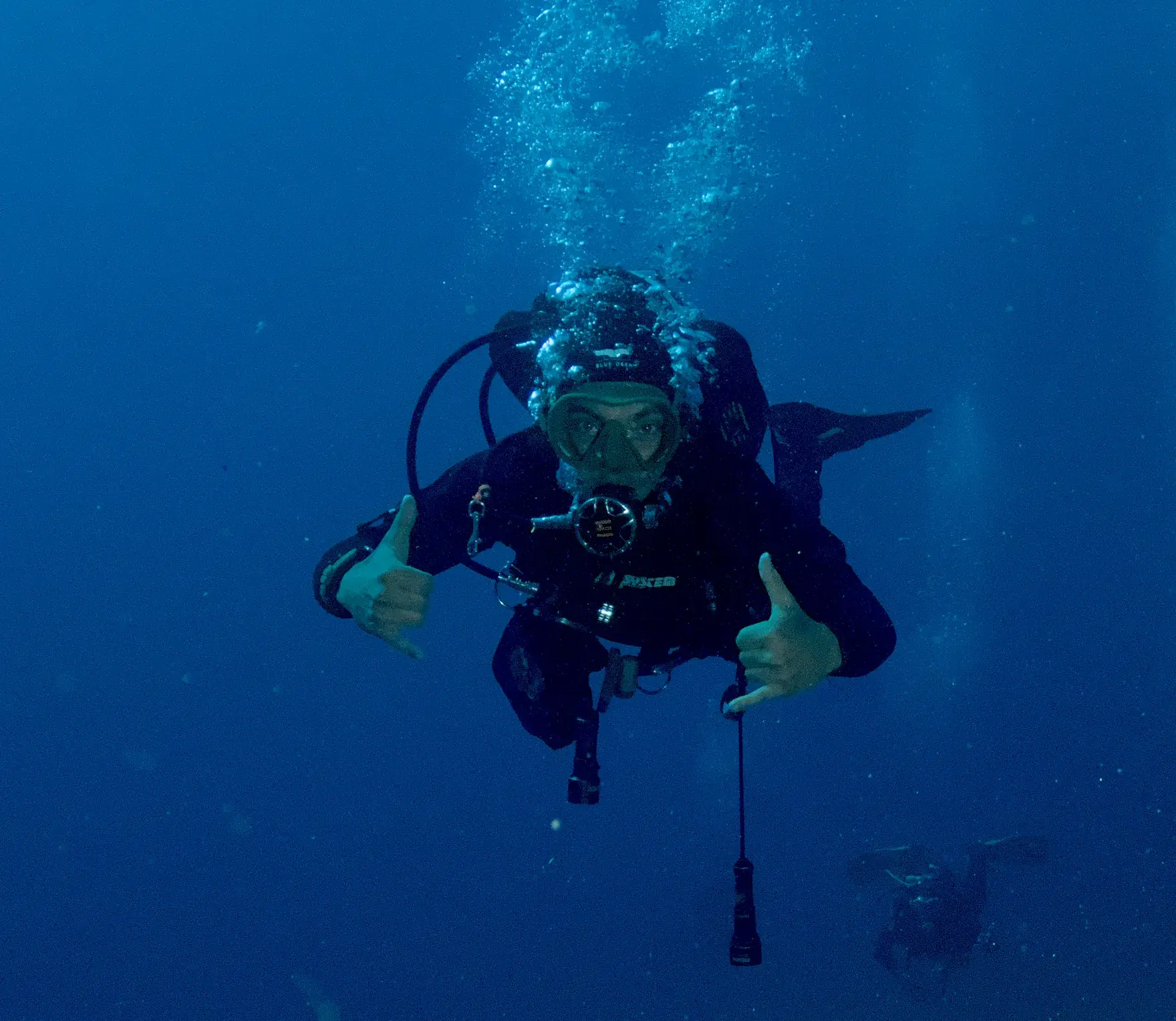 Orlando scuba diving in open blue water, throwing two shaka signs at the camera